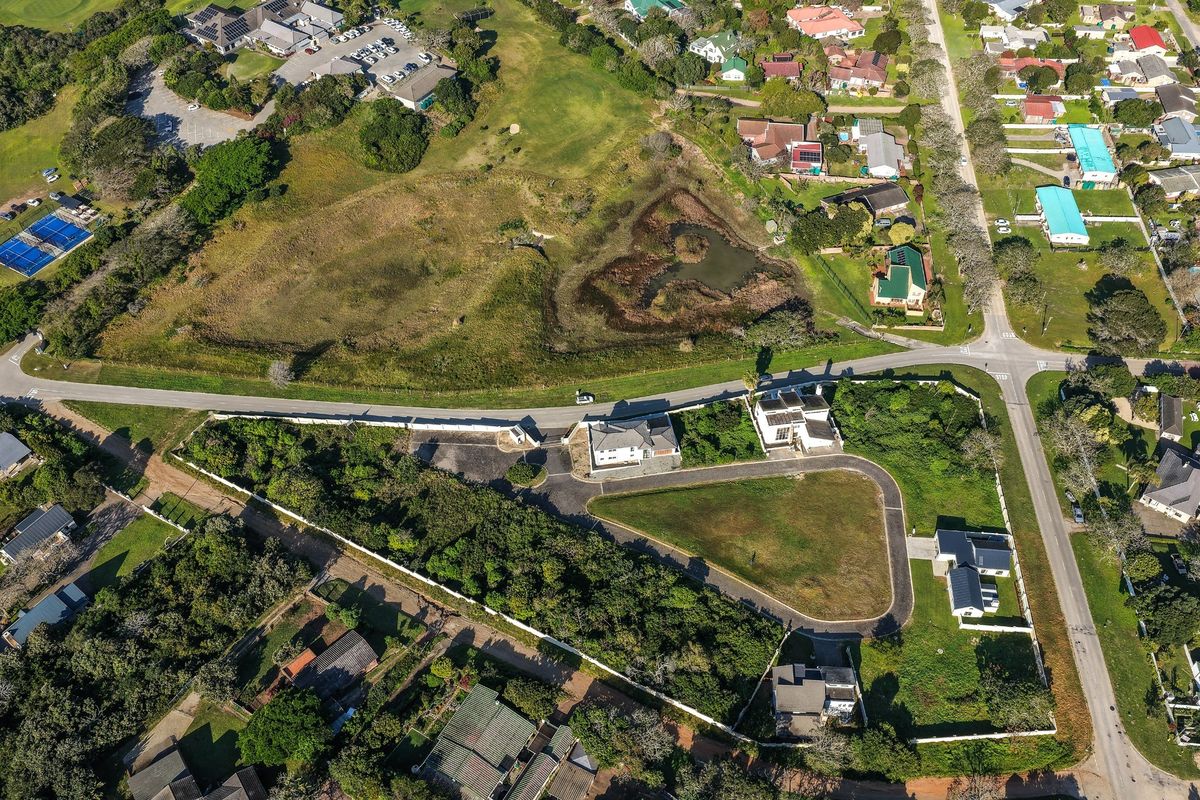 Aerial view of a residential vacant land plot featuring a paved driveway, established boundary walls, and surrounding greenery in a suburban neighborhood.