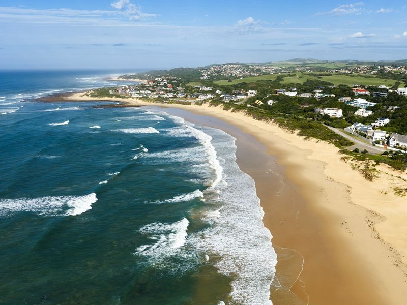 An aerial view of the coastal landscape, showcasing the expansive sandy beach, ocean waves, and the surrounding residential neighborhood.