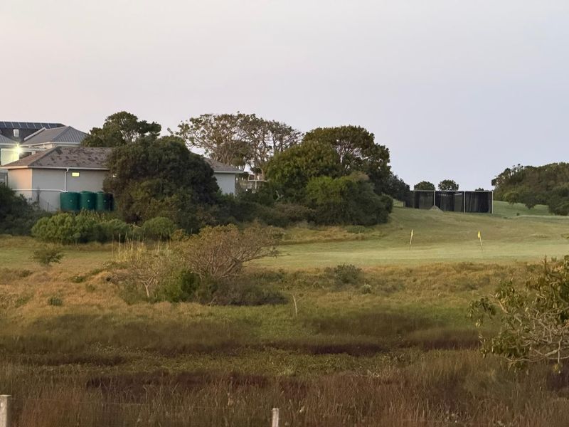A scenic view overlooking a golf course fairway with surrounding greenery and residential infrastructure in the distance.