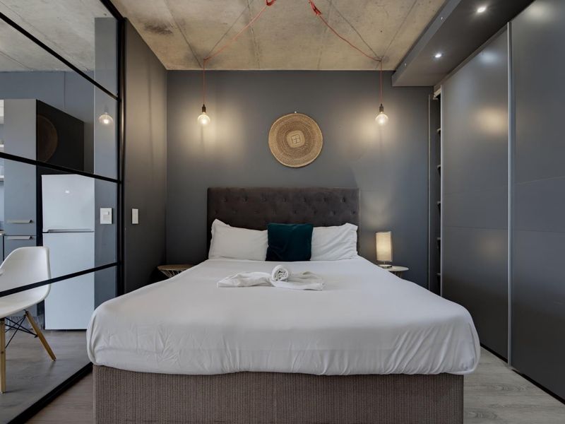Modern bedroom featuring an exposed concrete ceiling, sleek built-in wardrobes, and a contemporary glass partition wall separating the sleeping area.