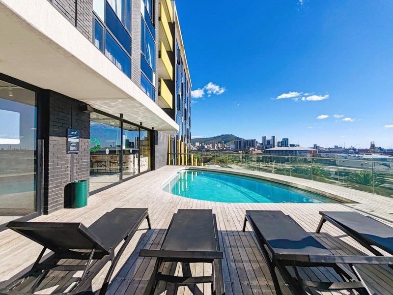 Modern rooftop pool area featuring timber decking, glass balustrades, and expansive city and mountain views.