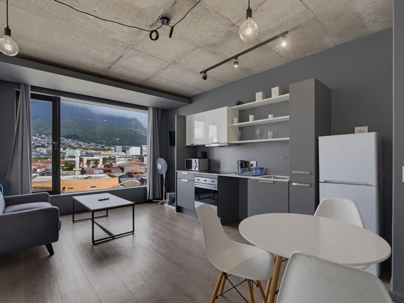 Modern open-plan living area featuring an exposed concrete ceiling, sleek cabinetry, and a large window offering expansive mountain and city views.