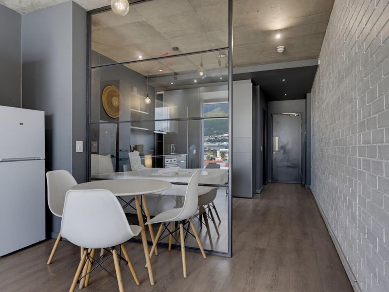 Modern open-plan apartment featuring an exposed concrete ceiling, industrial-style glass partition, and a contemporary kitchen area with sleek cabinetry.