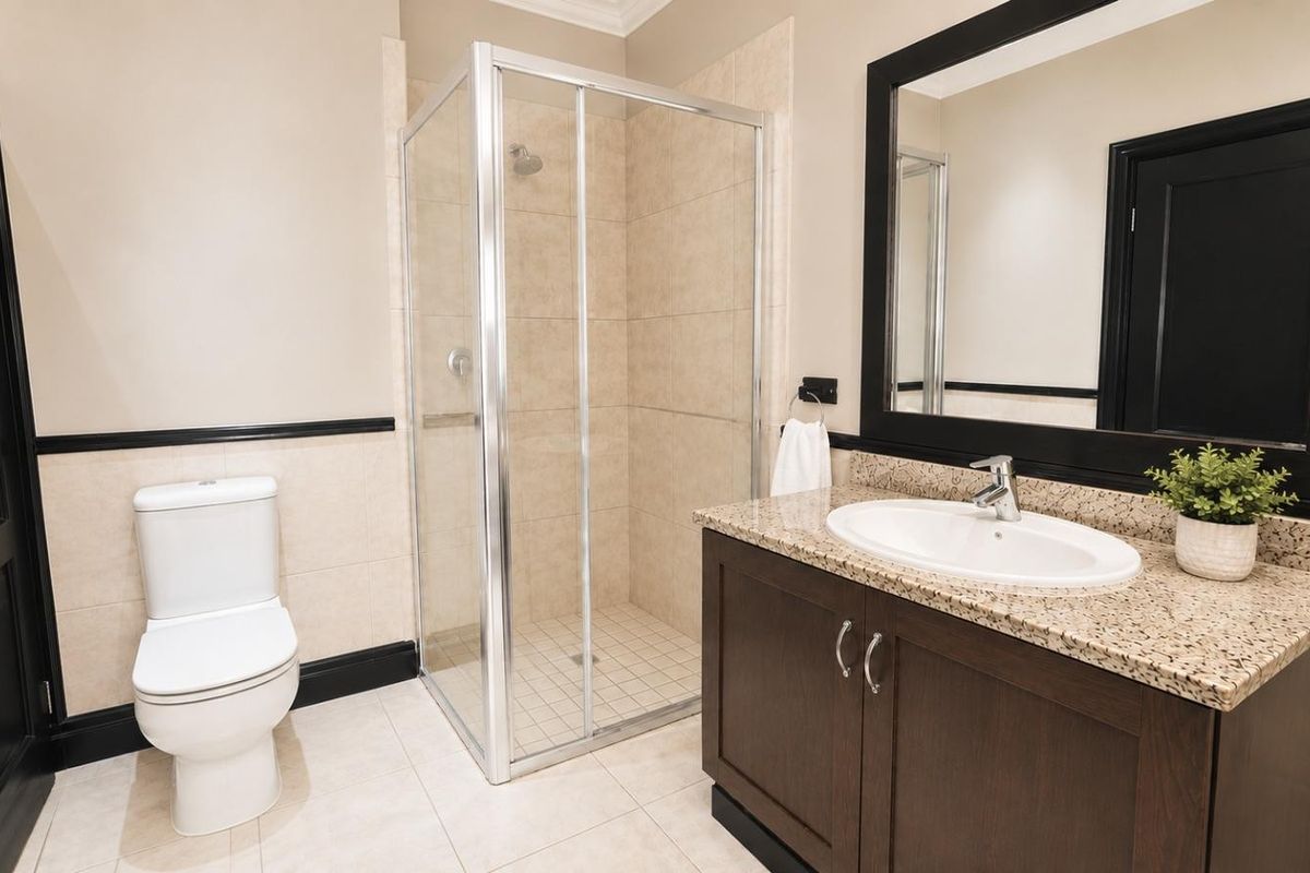 A well-maintained bathroom featuring a glass shower enclosure, a vanity with granite countertop, and neutral wall tiling with dark trim accents.