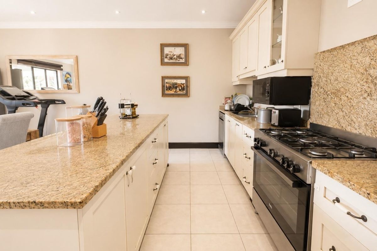 Spacious kitchen featuring a large granite-topped island, ample cabinetry, and a professional-style gas stove with integrated oven and extractor fan.