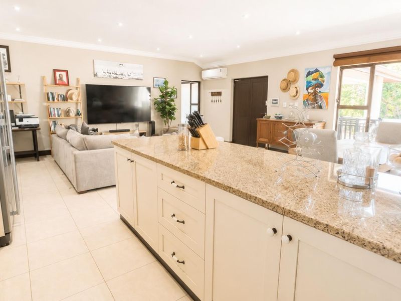 Spacious open-plan living area featuring a large granite-topped kitchen island, tiled flooring, and seamless flow to the outdoor patio through sliding glass doors.