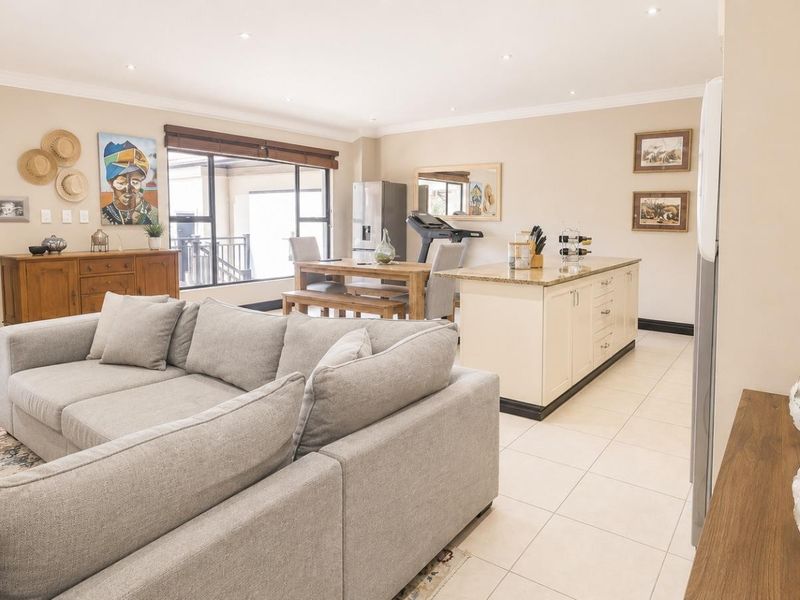 Spacious open-plan living and kitchen area featuring a central island with granite countertops, recessed lighting, and neutral tiled flooring throughout.