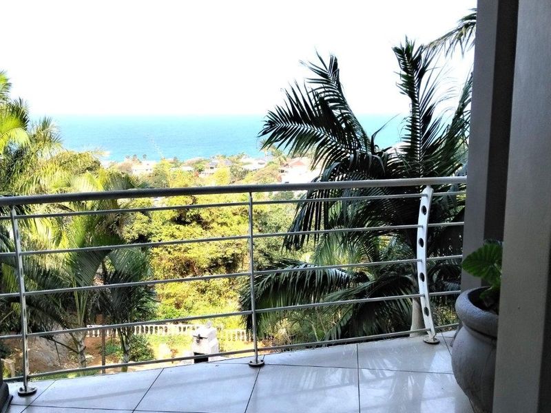 A covered balcony featuring tiled flooring and a modern stainless steel balustrade, offering scenic views of the surrounding greenery and the ocean.
