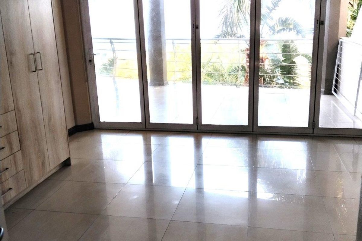 A bright, empty bedroom featuring modern tiled flooring, extensive built-in cupboards, and large sliding glass doors that open onto a private balcony.
