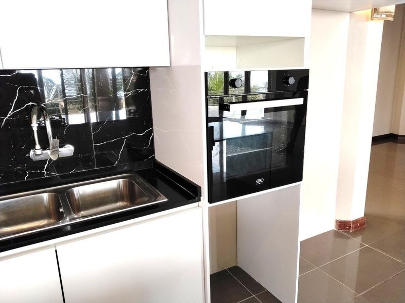 Modern kitchen area featuring white cabinetry, a built-in oven, and a double stainless steel sink with a striking black marble-effect splashback.