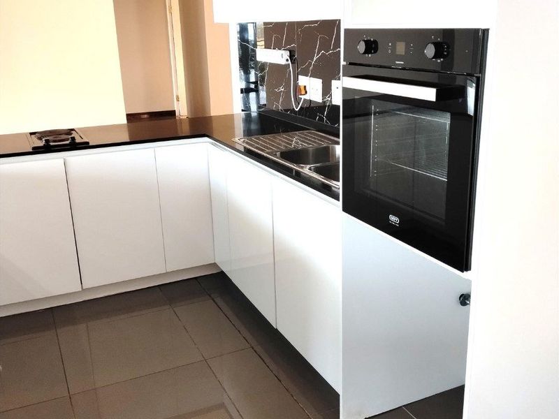 Modern kitchen featuring white cabinetry, black marble-look splashback, built-in oven, hob, and sleek tiled flooring in an open-plan layout.
