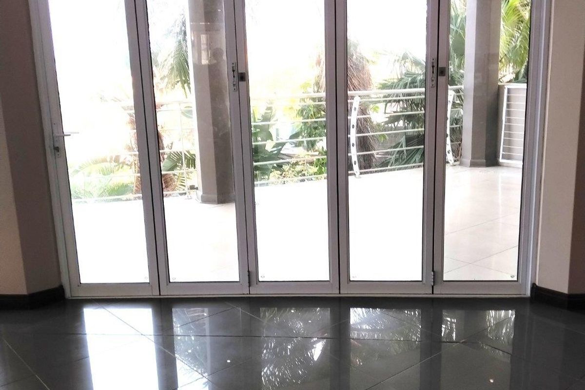 Spacious living area featuring high-gloss porcelain floor tiles and large aluminium stackable glass doors opening onto a covered patio.