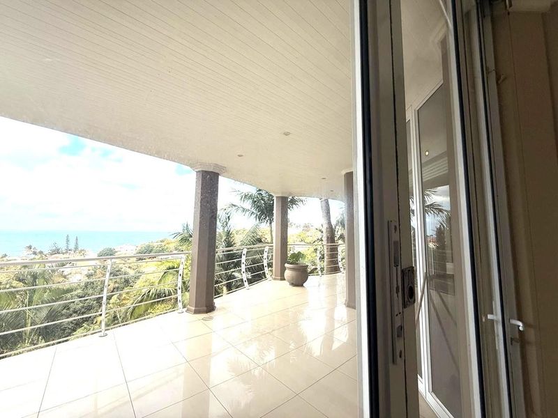 Spacious covered balcony featuring tiled flooring, structural columns, and a metal balustrade, offering expansive outdoor views.