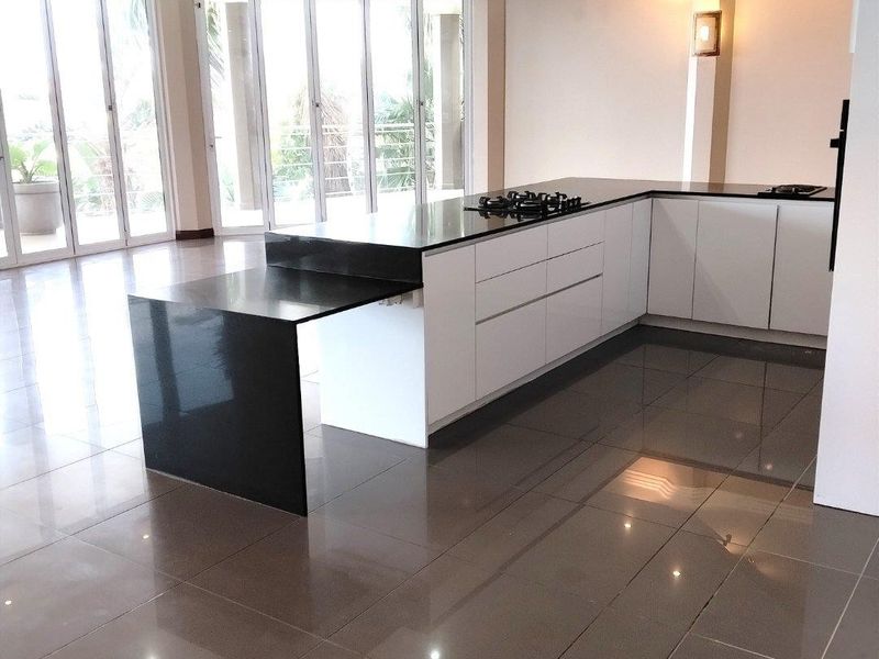 Spacious open-plan kitchen and living area featuring modern white cabinetry, black stone countertops, gas hob, and large sliding glass doors leading to the outdoors.