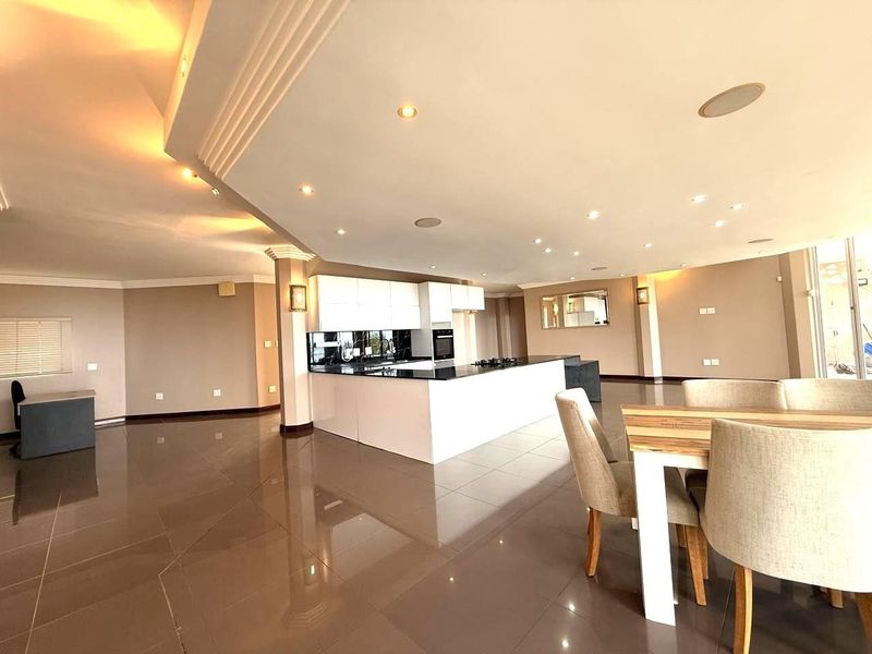 Spacious open-plan living and dining area featuring a modern kitchen with a central island, sleek cabinetry, and recessed ceiling lighting throughout.