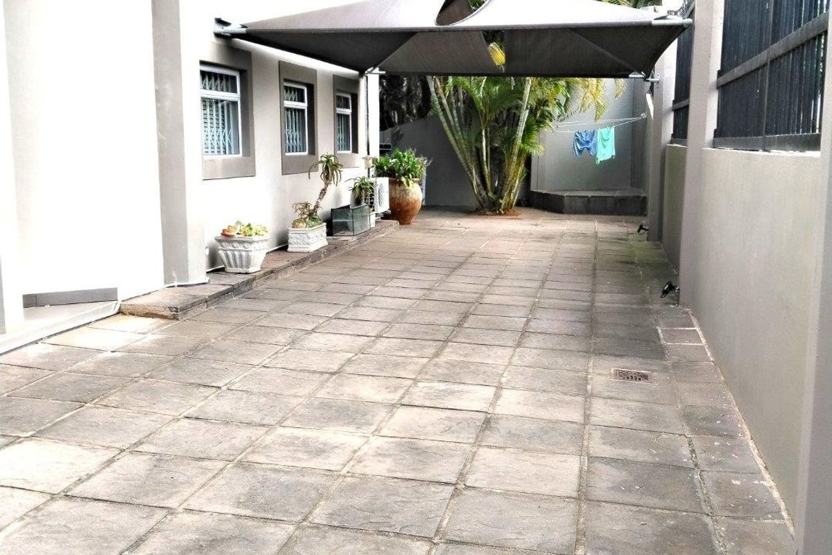A paved rear courtyard area featuring a shade sail, perimeter wall with security fencing, and exterior lighting.
