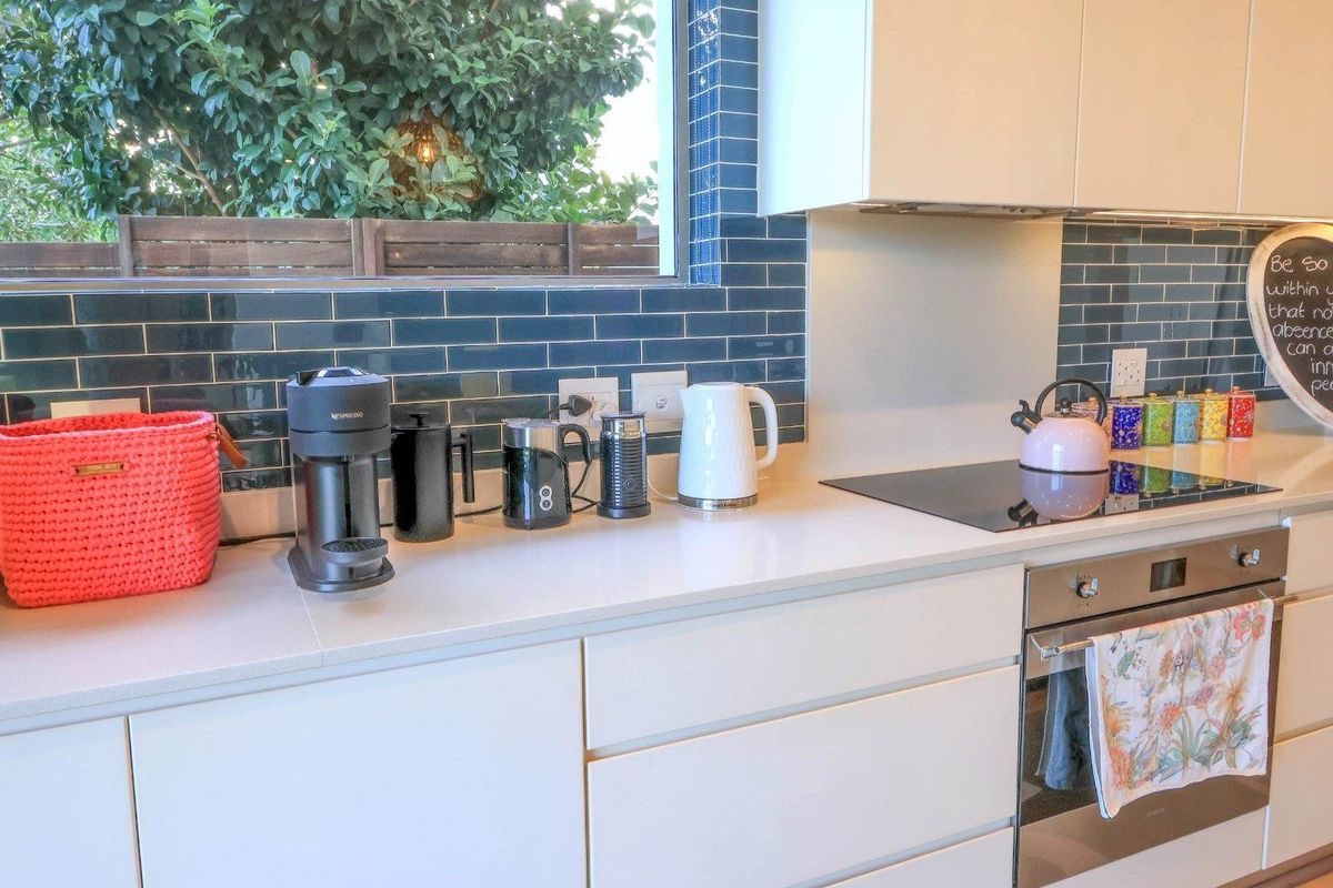 Modern kitchen featuring sleek handleless cabinetry, white quartz countertops, a dark blue subway tile backsplash, and a built-in oven with induction cooktop.