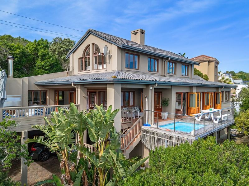 Rear view of a multi-level residence featuring a raised timber deck, a plunge pool, and extensive timber-framed glazing set within a lush garden environment.