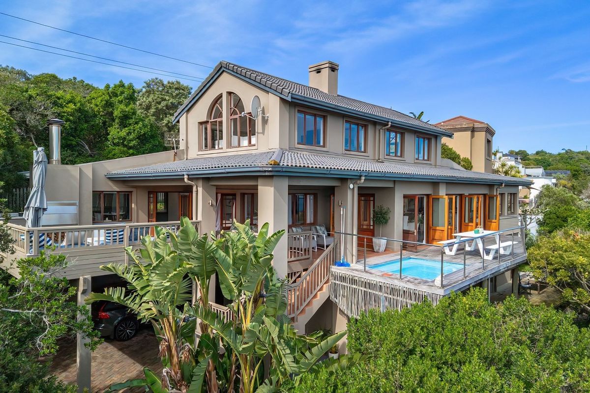 Rear view of a multi-level residence featuring a raised timber deck, a plunge pool, and extensive timber-framed glazing set within a lush garden environment.