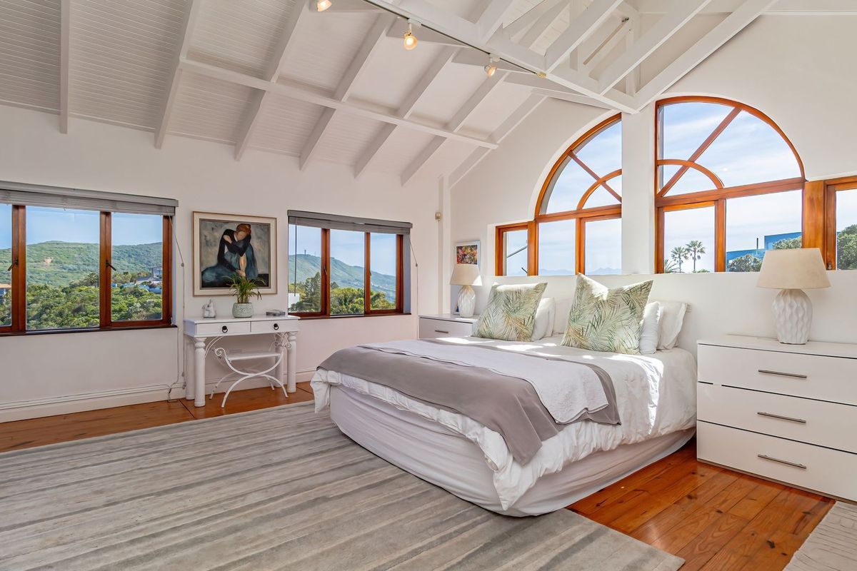 Spacious bedroom featuring a vaulted timber ceiling with exposed rafters, warm timber flooring, and large arched windows offering scenic hillside views.
