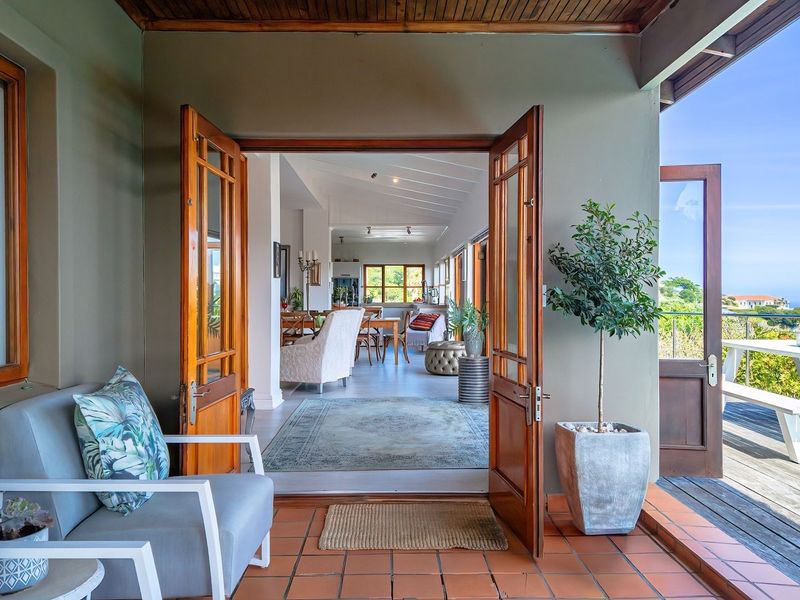 A covered patio featuring terracotta tiling and timber-framed doors, providing seamless indoor-outdoor flow to a wooden deck and swimming pool area.
