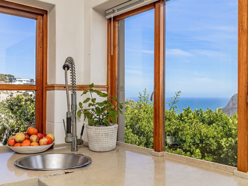 A bright kitchen sink area featuring stone countertops, a modern gooseneck faucet, and expansive timber-framed windows offering scenic coastal and ocean views.