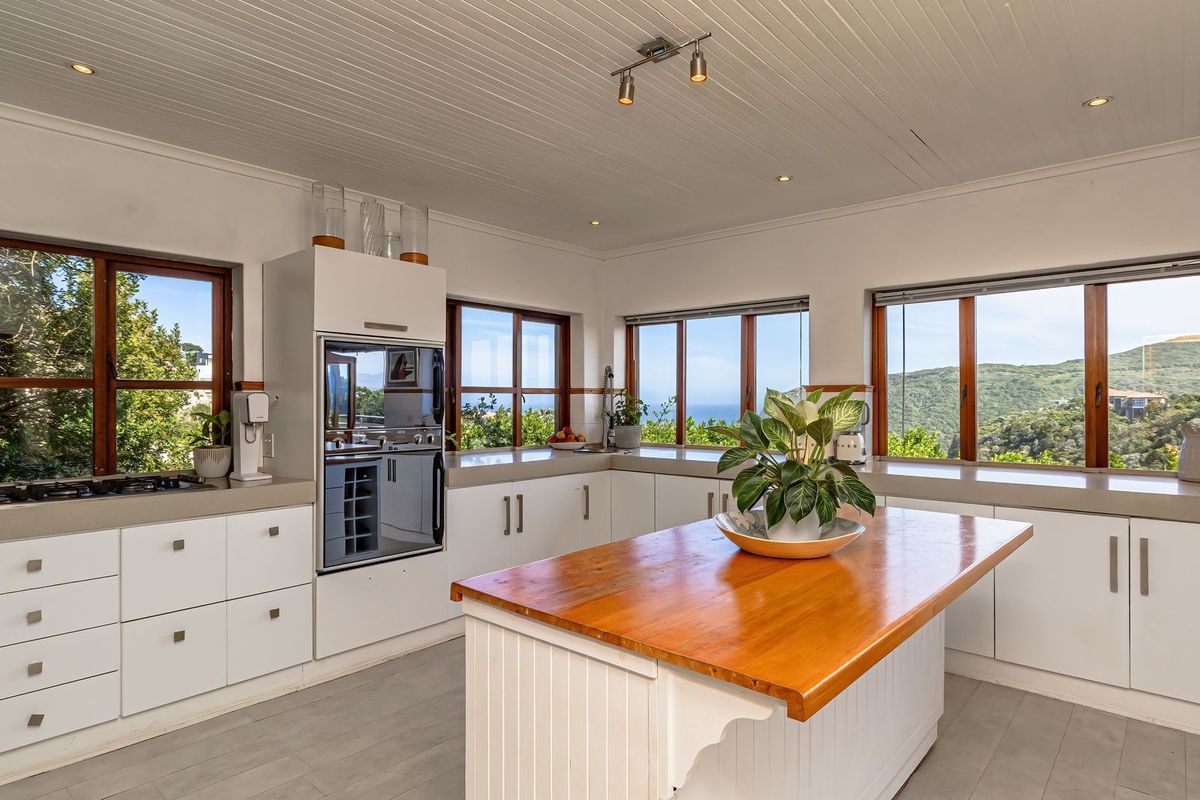 Bright kitchen featuring white cabinetry, stone and timber countertops, a central island, and expansive windows offering scenic coastal and mountain views.