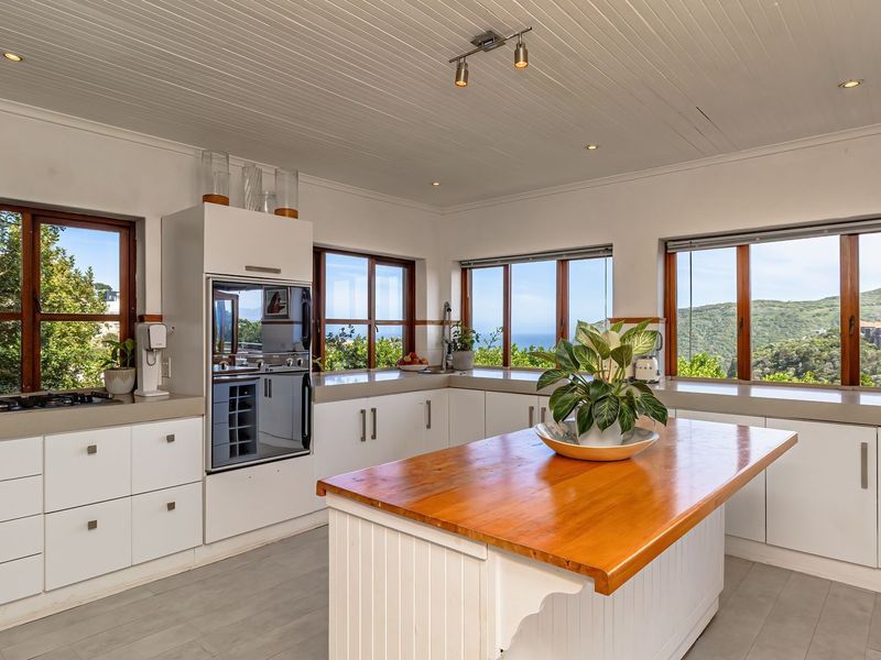 Bright kitchen featuring white cabinetry, stone and timber countertops, a central island, and expansive windows offering scenic coastal and mountain views.