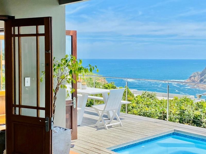 A scenic outdoor patio featuring timber decking, a glass balustrade, and a swimming pool with expansive ocean views.