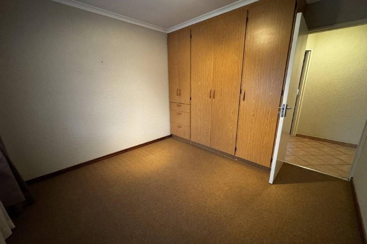 A vacant bedroom featuring built-in wooden cupboards, carpeted flooring, and coved ceilings, offering a blank canvas for potential updates.