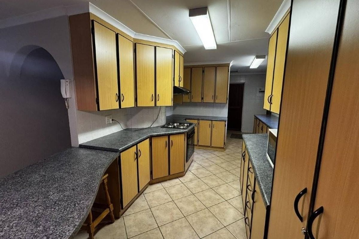 A functional kitchen featuring extensive laminate cabinetry, dark countertops, built-in oven, gas hob, and tiled flooring, offering a practical layout for renovation.