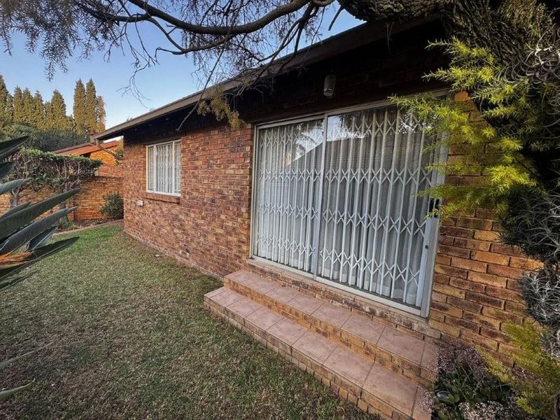 Rear exterior view of a face brick townhouse featuring a sliding glass door with security gate and a small tiled patio area.