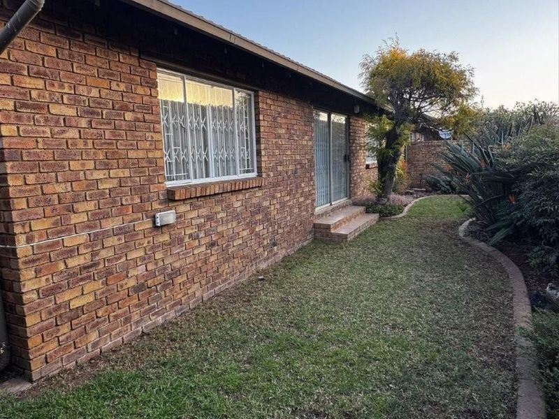 Rear view of the townhouse featuring a face brick facade, sliding door access, and a well-maintained garden area.