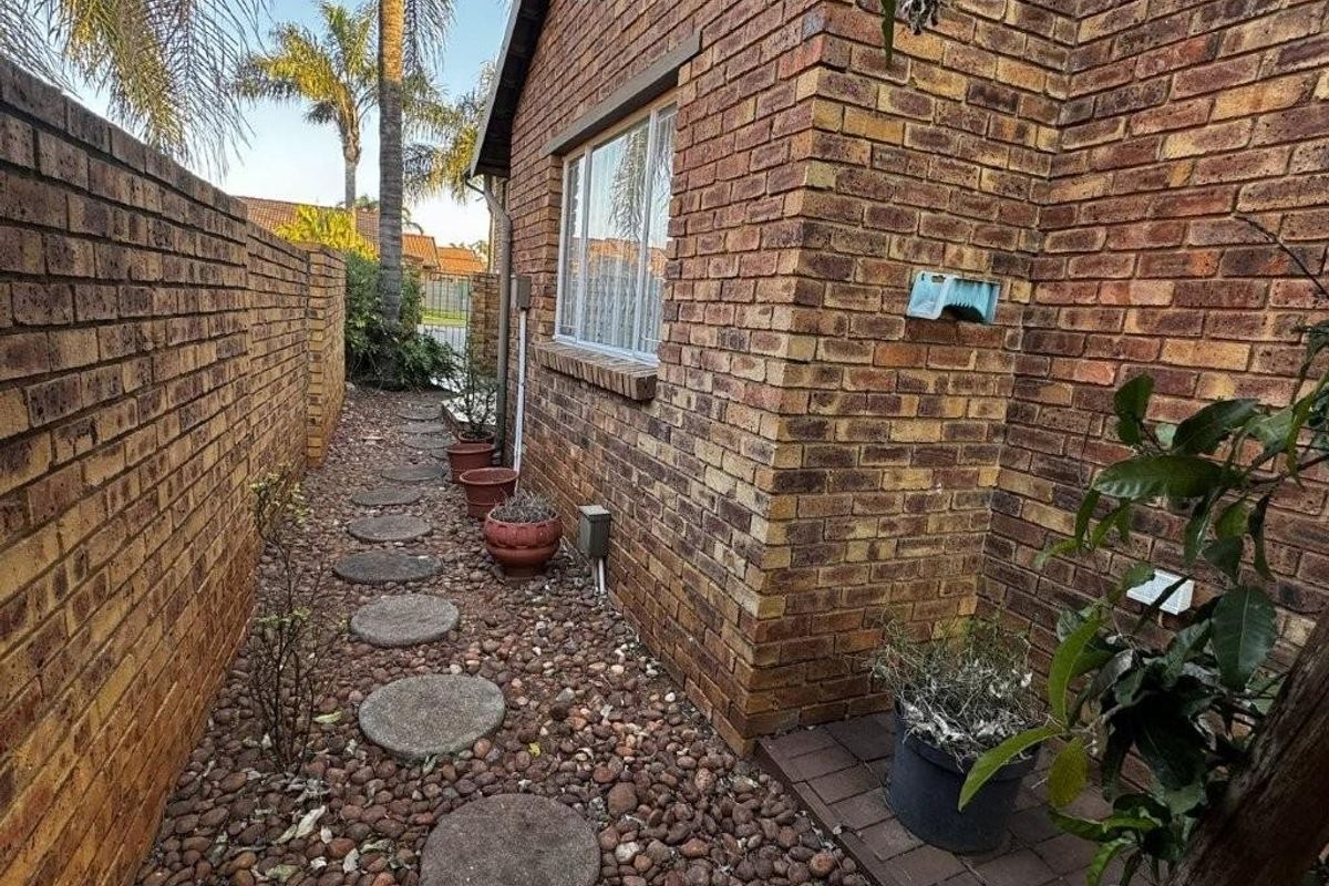 A side exterior view of the townhouse featuring face brick walls, a pebble-covered pathway with stepping stones, and a secure boundary wall.