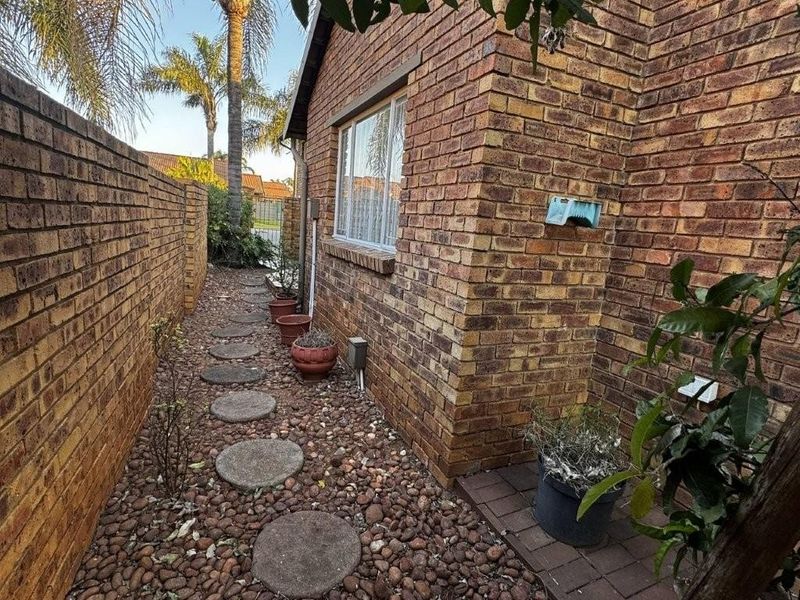 A side exterior view of the townhouse featuring face brick walls, a pebble-covered pathway with stepping stones, and a secure boundary wall.