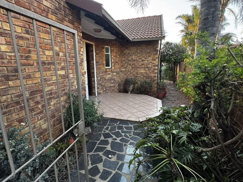 Front entrance of the townhouse featuring a face brick facade, tiled patio area, and a stone paved walkway leading to the front door.