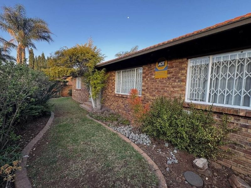 Front elevation of a face brick townhouse featuring security bars on windows and a well-maintained garden area.