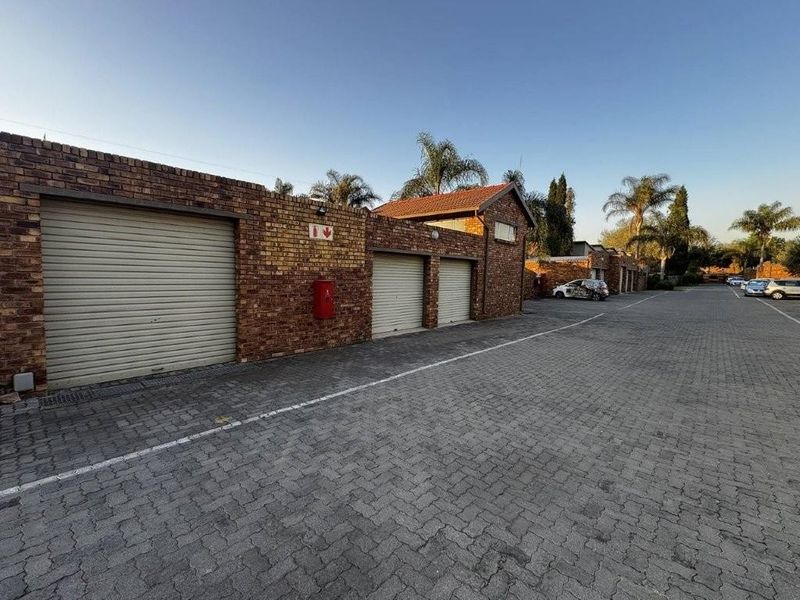 Exterior view of a townhouse complex featuring three individual roller shutter garage doors and paved driveway access.