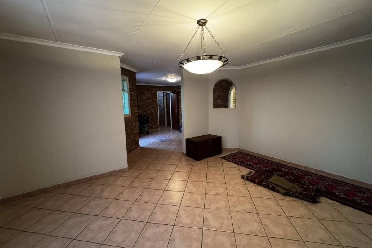 A spacious, empty living area featuring tiled flooring, coved ceilings, and a decorative brick-accented archway leading to an adjacent space.