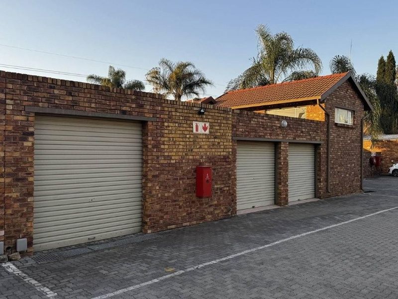 A well-maintained townhouse exterior featuring a face brick facade with three secure roller shutter garage doors and paved driveway access.