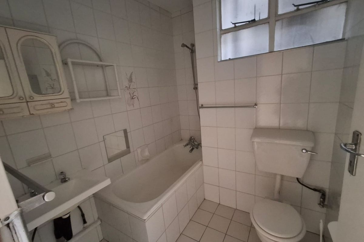 A dated bathroom featuring a standard bathtub, wall-mounted basin, and toilet with white tiled walls and flooring.