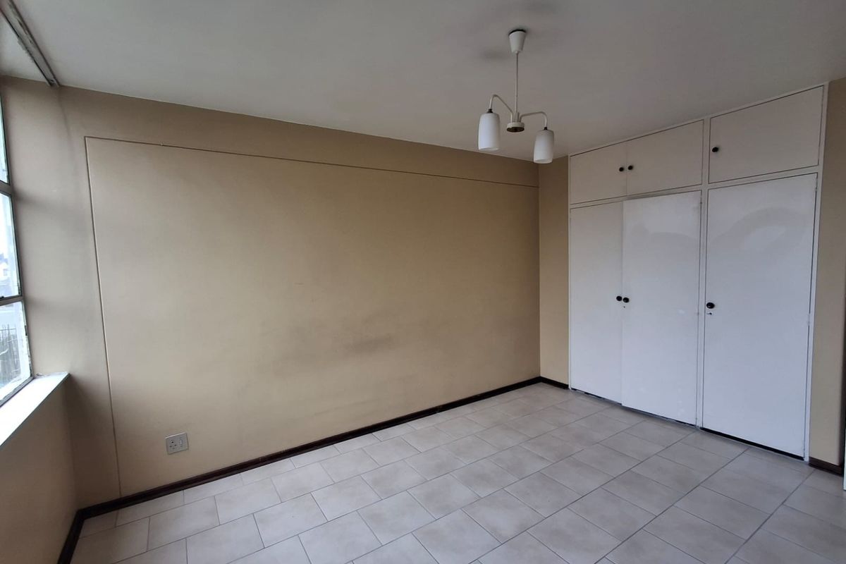 An empty bedroom featuring tiled flooring, built-in cupboards with overhead storage, and a central ceiling light fixture.