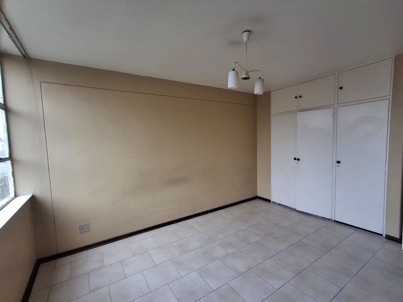 An empty bedroom featuring tiled flooring, built-in cupboards with overhead storage, and a central ceiling light fixture.