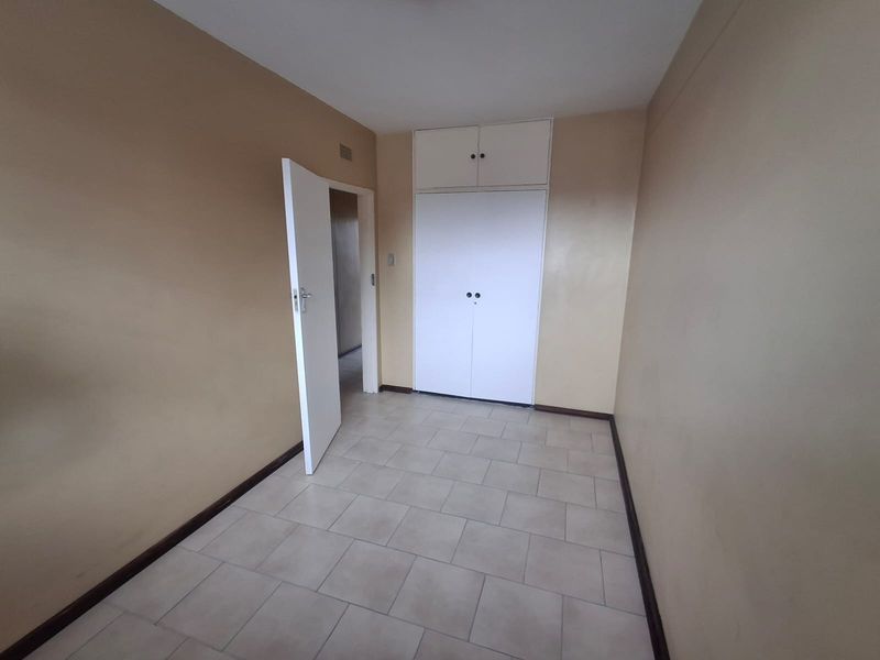 An empty bedroom featuring neutral wall paint, tiled flooring, and built-in storage cupboards with overhead cabinets.