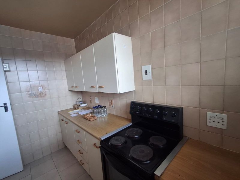 A functional kitchen featuring built-in cabinetry, laminate countertops, and a freestanding electric stove, finished with dated ceramic wall tiles.