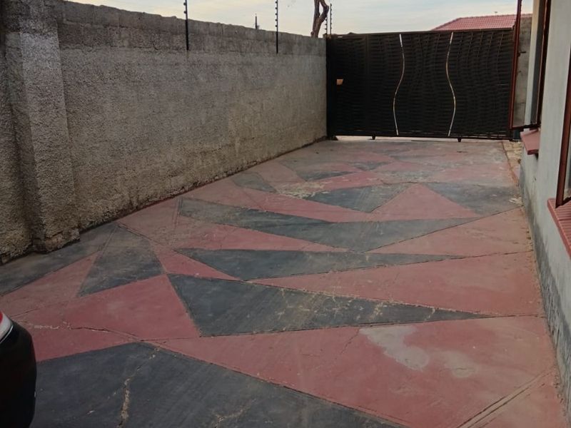 Front driveway area featuring a patterned paved surface, perimeter wall with electric fencing, and a secure sliding metal gate.