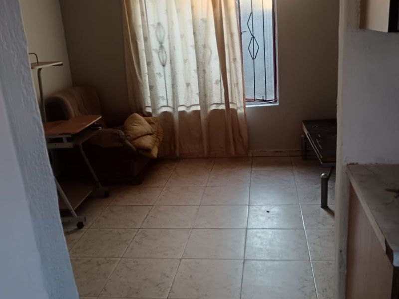 A modest living area featuring tiled flooring, a ceiling fan, and a window fitted with a security gate.
