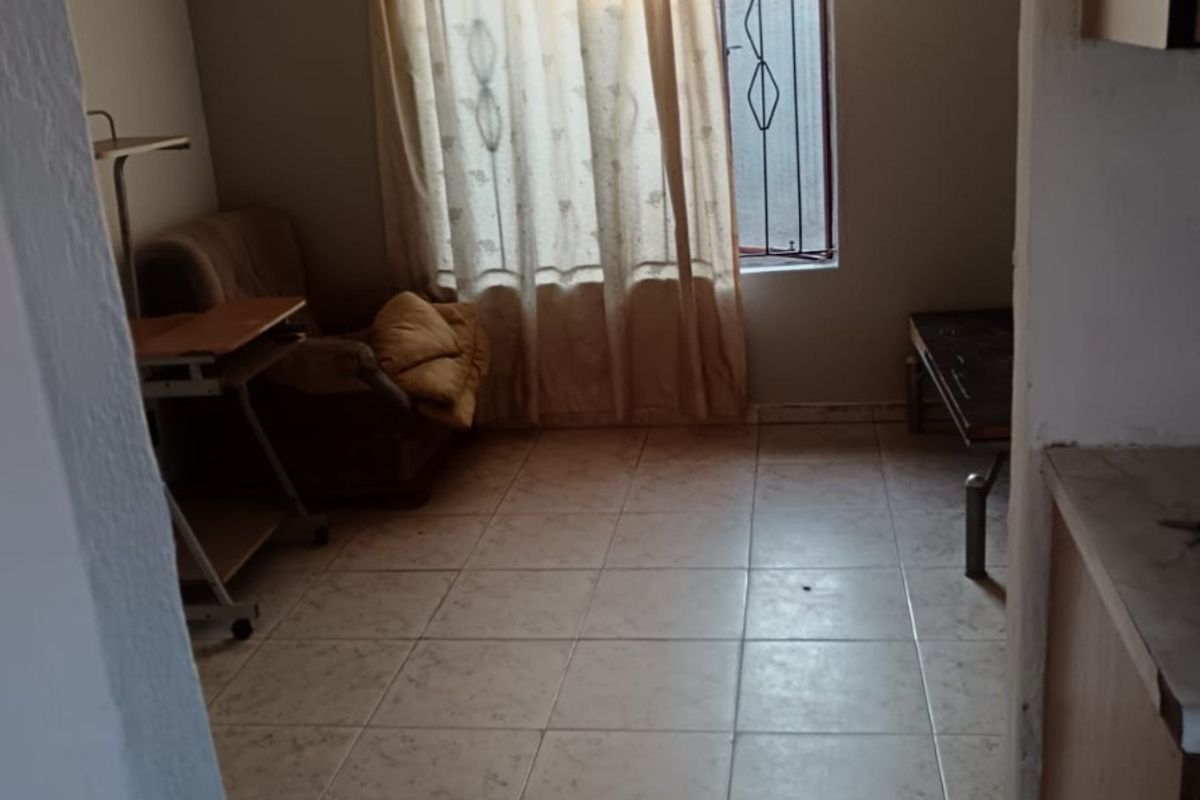 A modest living area featuring tiled flooring, a ceiling fan, and a window fitted with a security gate.