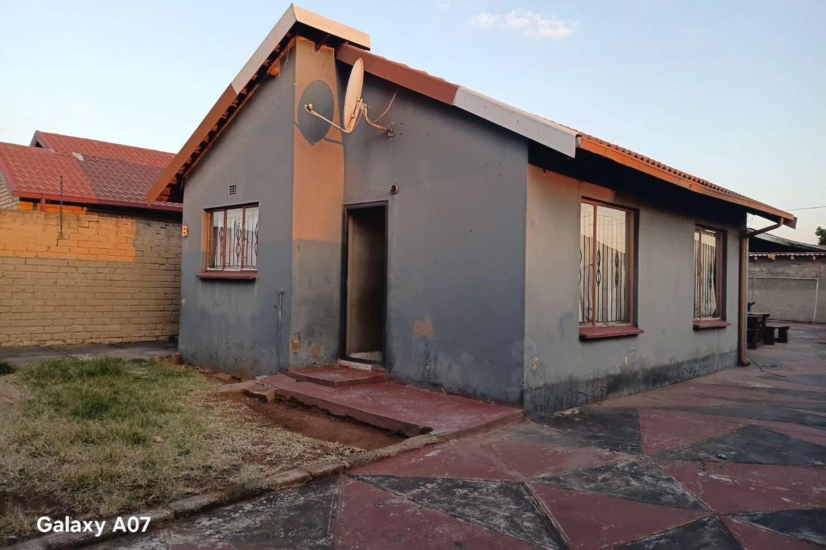 Rear view of a detached house featuring a tiled roof, security bars on windows, and a paved courtyard area.
