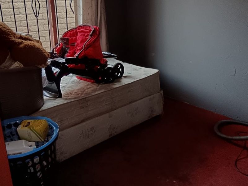 A bedroom featuring carpeted flooring and a window with a security gate, currently requiring cosmetic updates and maintenance.